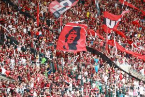 Excited soccer fans in red and black cheer at Maracanã Stadium, Rio de Janeiro.